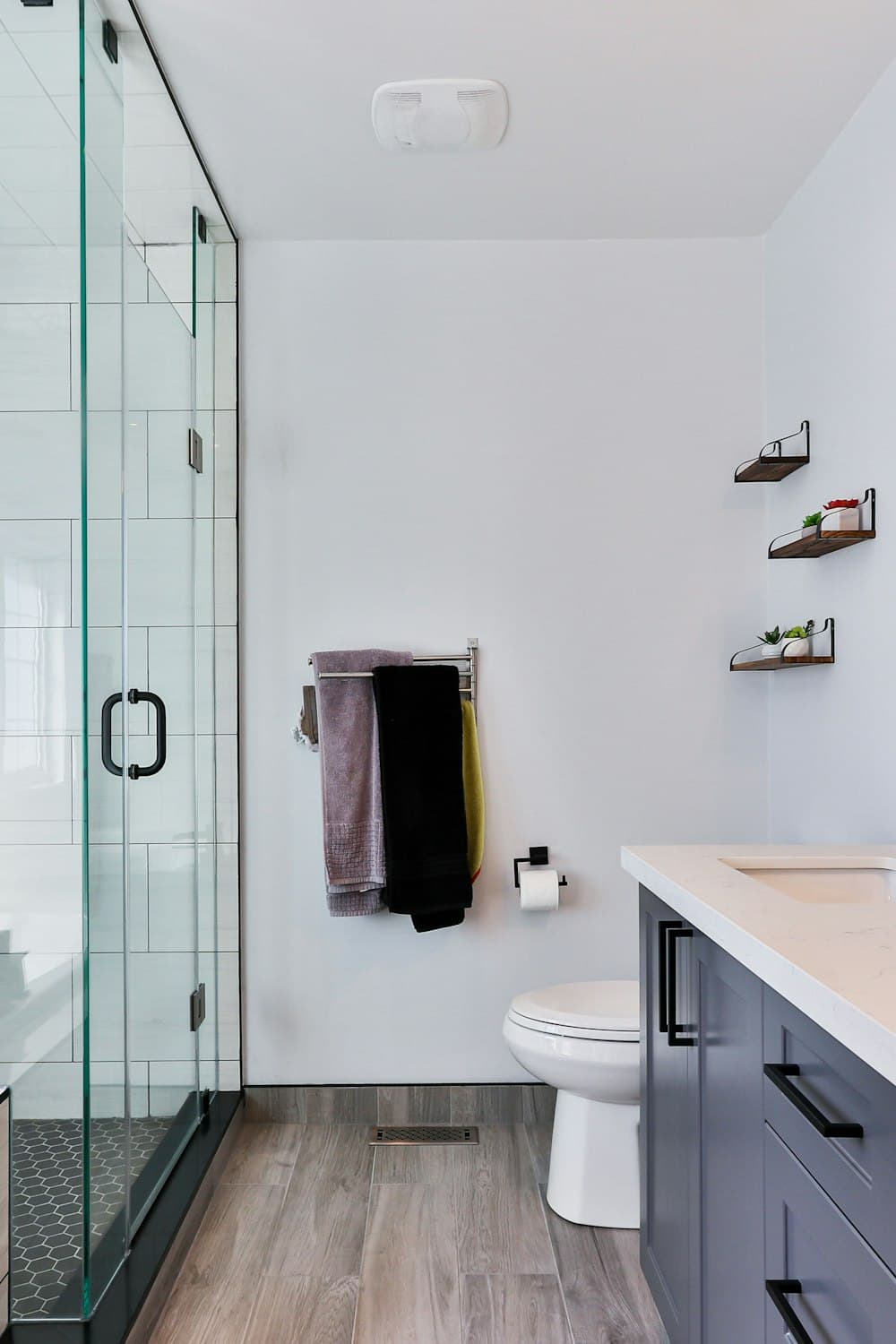 Portrait crop of a bright bathroom vanity with a dark cabinet and a glass shower